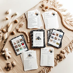 May include: A collection of wedding game cards with various designs and text, including "Over or Under," "Bridal Scattergories," and "Guess How Many." The cards are arranged on a beige surface with decorative elements.