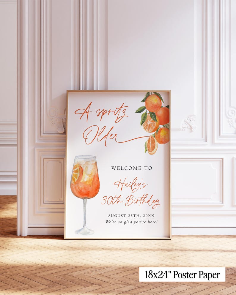 May include: A framed poster with watercolor illustrations of oranges and a cocktail. The text reads "A Spritz Older" and welcomes guests to Hailey's 30th Birthday on August 25th. The poster is 18x24 inches.