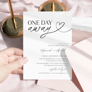 Op de afbeelding: Een witte uitnodigingskaart met zwart schrift met de tekst "ONE DAY away" met een hartsymbool. De kaart bevat details voor een repetitiediner, inclusief datum, tijd en locatie. De kaart ligt op een roze ondergrond.