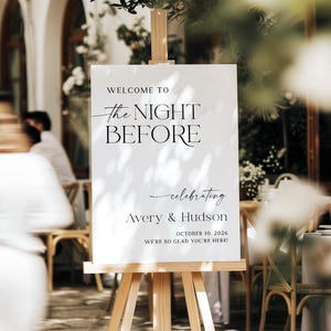 Pu&ograve; includere: Un cartello bianco su un cavalletto di legno con la scritta "WELCOME TO the NIGHT BEFORE celebrating Avery & Hudson OCTOBER 10, 2026 WE'RE SO GLAD YOU'RE HERE!" in nero. Il cartello &egrave; all'aperto.