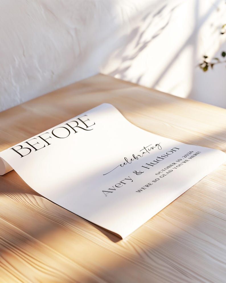 Pu&ograve; includere: Un foglio di carta bianco arrotolato con la parola "BEFORE" in un carattere nero grande ed elegante. La carta include anche il testo "celebrating Avery & Hudson October 10, 2026 WE'RE SO GLAD YOU'RE HERE!" su una superficie di legno.