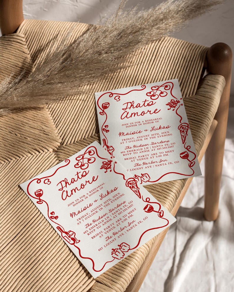 May include: Two white invitation cards with red text and illustrations. The text reads "Thato Amore" and "Join us for a rehearsal dinner in honor of Maisie & Lukas". The cards list the date, time, and location of the event. The illustrations include wine glasses, pizza slices, and peppers.