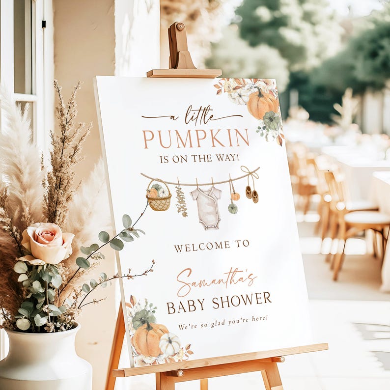 May include: A white rectangular baby shower sign on a wooden easel featuring the text A little PUMPKIN IS ON THE WAY! and Samantha's BABY SHOWER. The design includes watercolor illustrations of pumpkins, a clothesline with a onesie, and baby shoes.