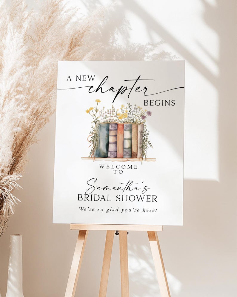 May include: A white sign on a wooden easel with the text "A New Chapter Begins" and "Welcome to Samantha's Bridal Shower". The sign features watercolor illustrations of books and flowers.