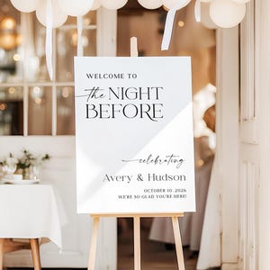 Pu&ograve; includere: Un cartello bianco su un cavalletto di legno con la scritta "WELCOME TO THE NIGHT BEFORE" e i nomi "Avery & Hudson" con la data 10 ottobre 2026. Palloncini bianchi e nastri decorano la parte superiore. Il cartello d&agrave; il benvenuto agli ospiti.