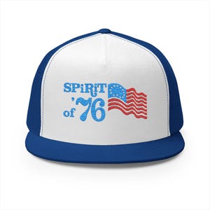 May include: A blue and white trucker hat featuring the text "Spirit of '76" and an embroidered American flag design. The hat has a blue brim and mesh back, and a white front panel.