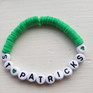 May include: A green and white beaded bracelet with the words "I love Patricks" spelled out in black letters. The bracelet is made of small, round beads and has a heart charm.