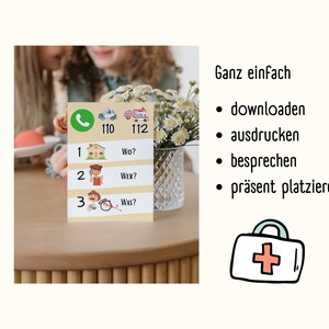 May include: A yellow card with a phone icon, a police car icon, and a fire truck icon. The numbers 110 and 112 are printed below the icons. The card also has three rows with numbers 1, 2, and 3. Each row has a question: "Wo?", "Wer?", and "Was?" The card is on a wooden table with a vase of white flowers.