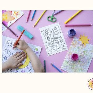 May include: A child's hand coloring a rocket ship on a white sheet of paper. The paper is on a pink surface with other coloring supplies, including colored pencils, markers, and paint.