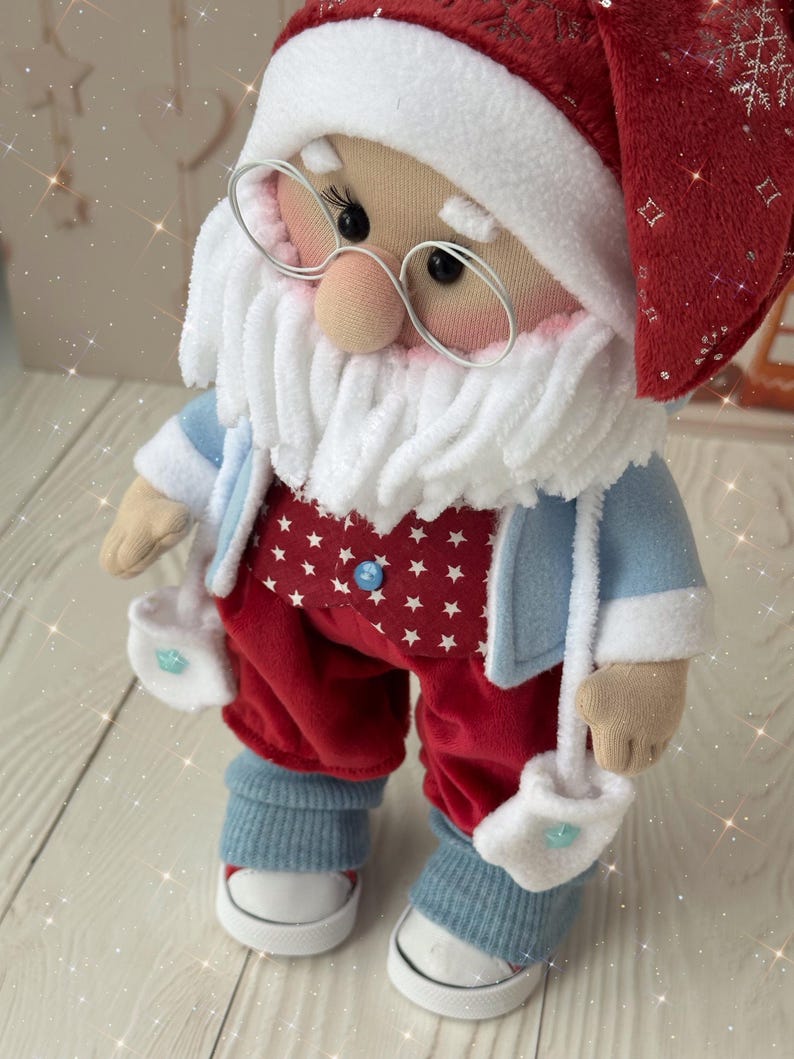 May include: A handmade Santa Claus doll wearing a red hat and pants with white star patterns, a blue jacket, and white mittens. The doll has a white beard, glasses, and blue sneakers. A festive Christmas decoration.