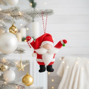 May include: A Santa Claus Christmas tree ornament. The ornament is red and white with a white beard and a red hat. The Santa Claus ornament is hanging from a red and white string on a Christmas tree.