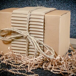 May include: A brown cardboard box tied with twine and wrapped in brown corrugated cardboard. The box is surrounded by brown packing paper.