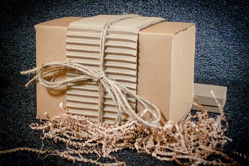 May include: A brown cardboard box tied with twine and wrapped in brown corrugated cardboard. The box is surrounded by brown packing paper.