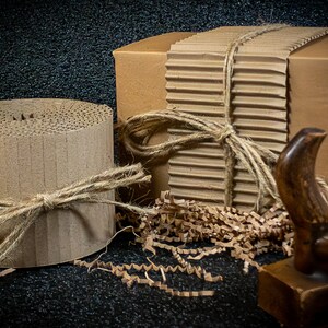 May include: Two cardboard boxes wrapped in brown paper and tied with twine. One box is round and the other is rectangular. Both boxes are surrounded by brown packing paper.