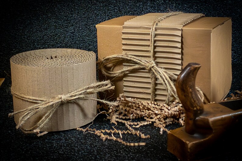 May include: Two cardboard boxes wrapped in brown paper and tied with twine. One box is round and the other is rectangular. Both boxes are surrounded by brown packing paper.