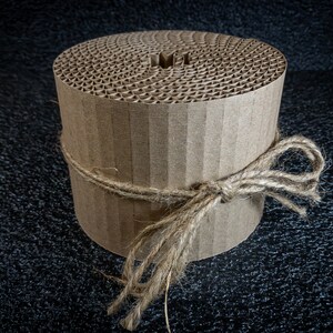 May include: A roll of brown corrugated cardboard tied with twine. The cardboard is in a spiral shape and has a hole in the center.