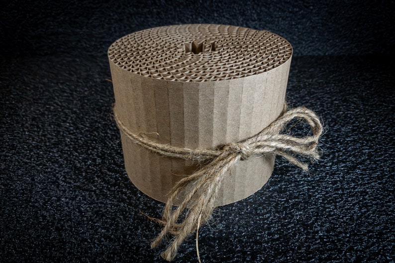 May include: A roll of brown corrugated cardboard tied with twine. The cardboard is in a spiral shape and has a hole in the center.