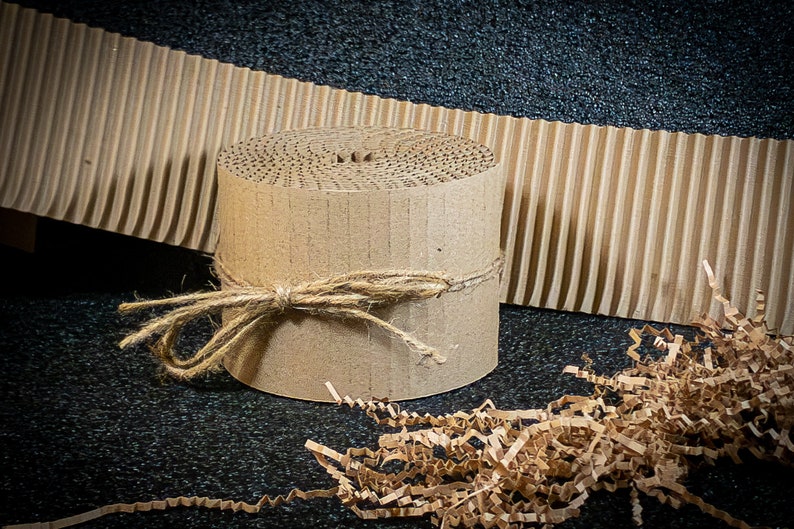May include: A roll of brown corrugated cardboard, tied with twine, and surrounded by brown packing paper shreds.