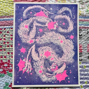 May include: A fantasy art print featuring a creature with a long, flowing body and a wolf-like head. The artwork is primarily purple and white, with bright pink star-shaped accents. The background is a dark blue, creating a celestial theme.