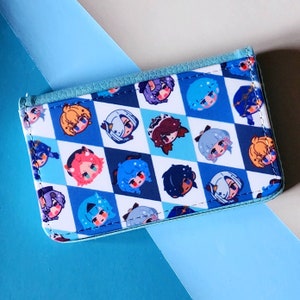 May include: A blue and white wallet with a repeating pattern of cartoon character faces. The wallet has a light blue trim and a snap closure. The background is a light blue and white surface.
