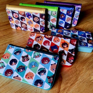 May include: A collection of colorful wallets with a diamond pattern and cartoon character illustrations. The wallets feature various colors, including gold, green, blue, purple, and red. The wallets are made of a smooth material and have a rectangular shape.