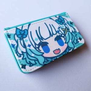 May include: A rectangular, bi-fold wallet featuring a cartoon anime character with blue hair and eyes. The wallet has a white background with a blue and white pattern, and a teal border. The character has a smiling expression.