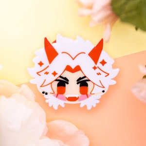 May include: A white and red anime-style character pin with a smiling face, red horns, and star accents. The pin has a cartoonish design with black eyes and pink cheeks. The background is a soft yellow and peach color with white flowers.