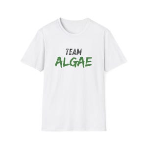 May include: A white short-sleeved t-shirt featuring the text "TEAM ALGAE" printed on the chest. The word "TEAM" is in a distressed black font, while the word "ALGAE" is in a bold, brush-stroke style green font across the center of the shirt.