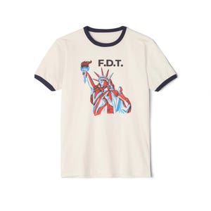 May include: A white t-shirt with a navy blue ringer neckline featuring a red, white, and blue illustration of the Statue of Liberty and the text "F.D.T."