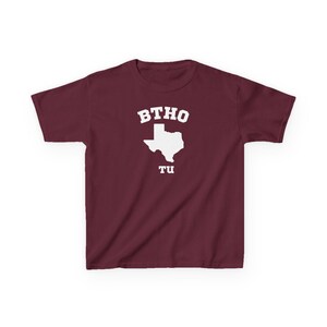 May include: A maroon t-shirt with the white text "BTHO" above a white outline of the state of Texas, and the text "TU" below the state outline. The t-shirt has short sleeves and a crew neck.