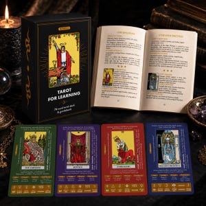 May include: A black box labeled Tarot for Learning with a 78-card deck and guidebook, featuring an open book displaying The Magician and The High Priestess cards, alongside four individual tarot cards: The Empress, Justice, Strength, and The High Priestess.