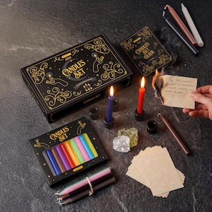 May include: A candle set with a black box featuring gold accents and the words "Candles Set". The set includes various colored candles, a guide, and other accessories. Two candles are lit, one blue and one red.