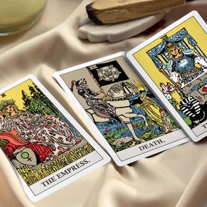 May include: Three tarot cards featuring The Empress, Death, and The Chariot. The Empress card shows a figure in a patterned robe, Death depicts a skeleton on a white horse, and The Chariot shows a figure in armor. Each card has a white border.