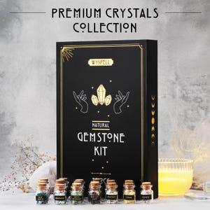 May include: A black box set labeled "Premium Crystals Collection" and "Natural Gemstone Kit" with gold accents. The set includes small glass bottles with cork stoppers, each labeled with a different gemstone name. A lit candle is in the background.