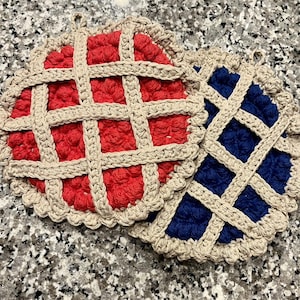 May include: Two crocheted pot holders in the shape of pies. One is red with a tan lattice top, and the other is blue with a tan lattice top. Both have a tan scalloped edge and a loop for hanging.