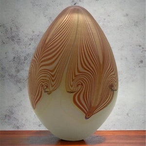 May include: A white glass egg-shaped vase with brown and white striped patterns. The vase is sitting on a wooden surface.