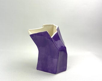 May include: A purple ceramic vase with a geometric design. The vase has a unique, angular shape and a glossy finish.