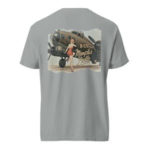 Puede incluir: Camiseta gris con una ilustración vintage de un bombardero B-17F y una mujer con un vestido rojo. El texto "B-17F Memphis Belle" está impreso en el diseño. La camiseta está hecha de un material suave y cómodo.
