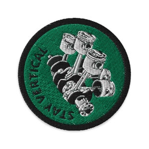 May include: An embroidered patch in green and black featuring a stylised image of a car engine with the text "STAY VERTICAL".