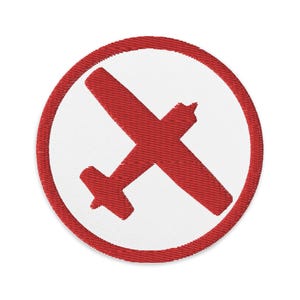 May include: Circular embroidered patch with a red aeroplane design inside a white circle, edged with a red border. The patch has a textured finish, ideal for attaching to garments or accessories.