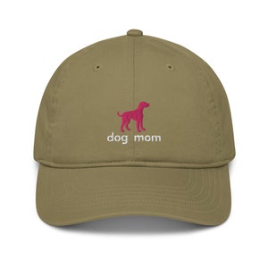 May include: A khaki green baseball cap with an embroidered pink dog silhouette and the text "dog mom" in white.