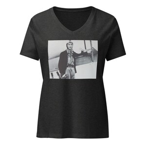 May include: A dark grey v-neck t-shirt with a black and white photo of a woman wearing a pilot's helmet and jacket standing next to an airplane.