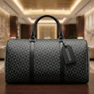 Könnte beinhalten: Eine schwarz-graue Reisetasche mit geometrischem Muster, einem oberen Griff und einem Gepäckanhänger mit der Aufschrift "ALEXANDER". Die Tasche besteht aus strapazierfähigem Material und ist für Reisen geeignet.