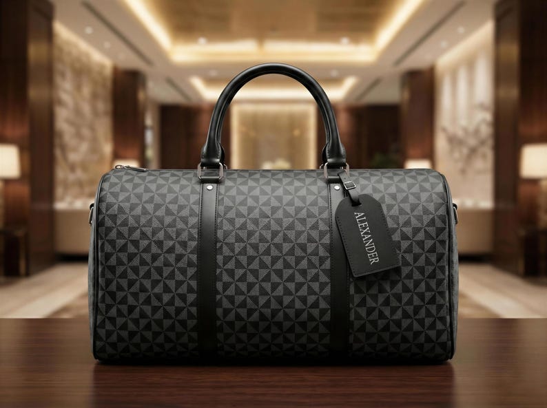 A black duffel bag with a geometric pattern and the name "Alexander" printed on it, placed on a wooden surface.