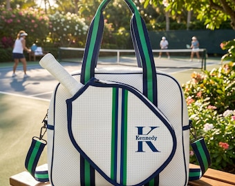 May include: A white perforated pickleball bag with navy blue and green striped webbing straps. The bag features a front pocket shaped like a pickleball paddle, personalized with a large navy blue letter K and the name Kennedy printed below it.
