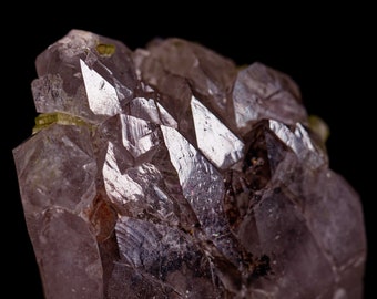 May include: Close-up of a cluster of amethyst crystals with sharp, pointed terminations. The crystals have a translucent, purplish-gray hue, with areas of light reflection. The background is solid black, highlighting the crystal's texture and form.