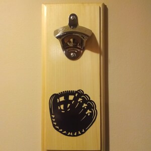 May include: A wooden wall mounted bottle opener with a baseball glove silhouette. The bottle opener is silver and has a chrome finish.