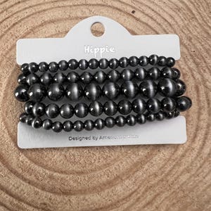 May include: A set of six black beaded bracelets with a shimmery finish. The bracelets are packaged on a white card with the word "Hippie" printed on it. The card also says "Designed by American artists".