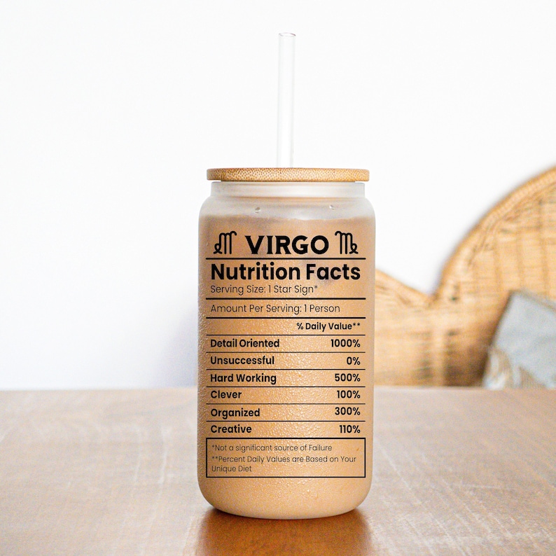 Op de afbeelding: Een doorzichtige glazen beker met een bamboe deksel en rietje. De beker heeft een zwart-witte afbeelding met de tekst "VIRGO Nutrition Facts" met een lijst van persoonlijkheidstrekken en hun overeenkomstige percentage dagelijkse waarden.
