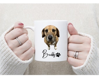 May include: White ceramic mug with a photo of a brown and white dog printed on it. The dog is looking at the camera. The mug has the word "Buddy" and a paw print printed on it.